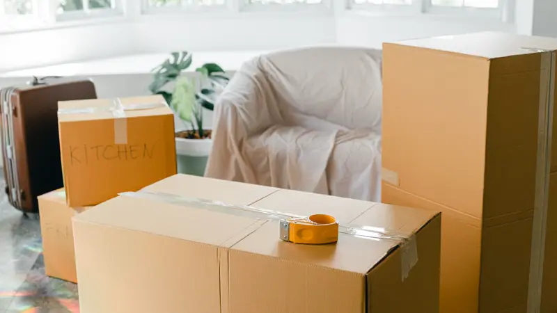 Packed moving boxes and a suitcase in a bright, empty living room