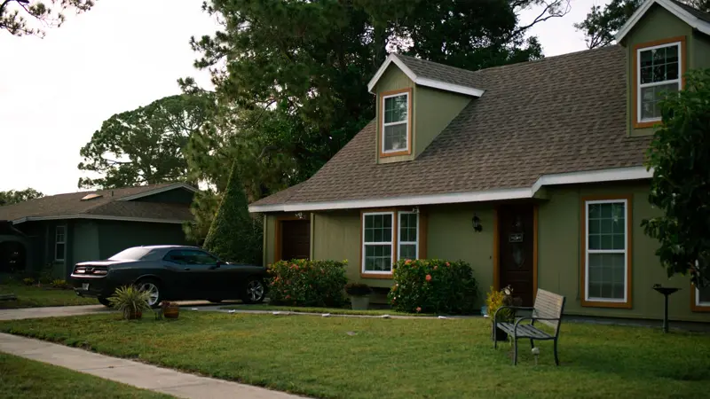 A two-story suburban house with a green front lawn and a car in the driveway
